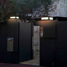 there are three black toilets in front of a brick wall with trees and bushes behind them