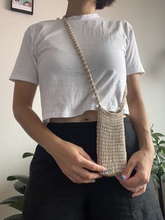 a woman wearing a white crop top and black pants holding a beige chain - wrapped purse