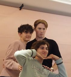 three young men standing next to each other in front of a pink wall with writing on it