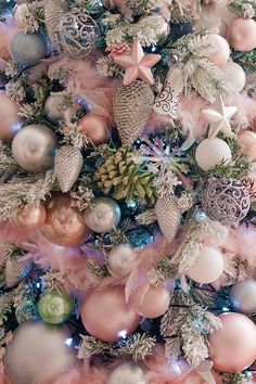 a christmas tree decorated with pink and silver balls, pine cones, ornaments and feathers