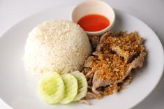 a white plate topped with rice and meat next to a small bowl of dipping sauce