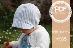 a baby wearing a blue and white striped hat sitting in the grass holding a piece of food