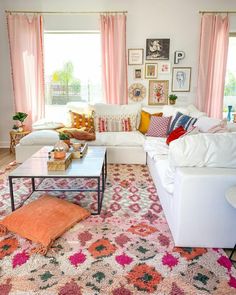 a living room filled with white couches and pink curtains on the windowsills