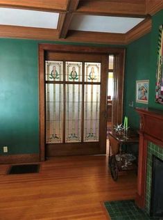 a living room with green walls and wood floors, fireplace in the corner and stained glass panels on the front door