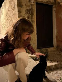 a woman kneeling down petting a black cat