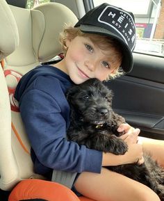 a young boy sitting in the back seat of a car holding a small black dog