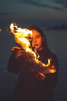 a woman holding a lit object in front of her face with flames coming out of it