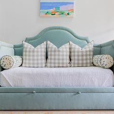 a blue daybed with pillows on it in the corner of a room next to a painting