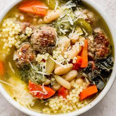 a white bowl filled with meatball soup and veggies on top of it