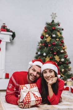 a man and woman laying on the floor in front of a christmas tree with presents