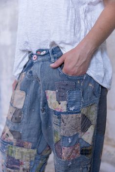 a man with his hand on his hip, wearing patchwork jeans and white t - shirt