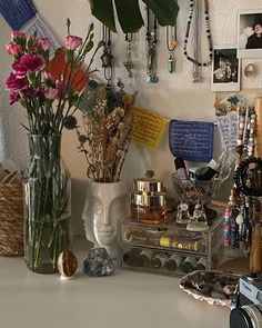 a white table topped with lots of jewelry and vases filled with flowers next to a camera