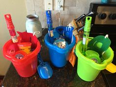 three buckets with spoons and toothbrushes in them sitting on a counter