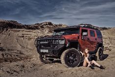 a woman sitting on the ground next to a red jeep