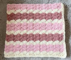 a pink and white crocheted blanket sitting on top of a gray carpeted floor