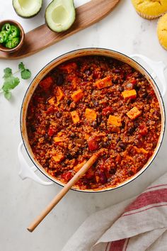 a large pot filled with chili next to bread and avocado on the side