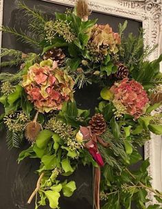 a wreath is hanging on the front door with pine cones and greenery around it