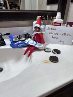 an elf is sitting on the sink with cookies and toothpaste