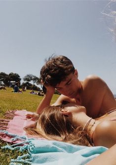 a man and woman laying on top of a blanket in the grass next to each other