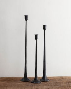 three black candlesticks on a wooden table