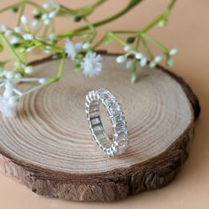 a silver ring sitting on top of a piece of wood next to some white flowers