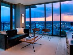 a living room filled with furniture and large windows overlooking the city at sunset or dawn