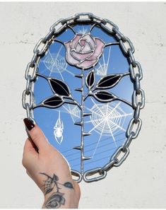 a person's hand holding up a stained glass mirror with a rose on it