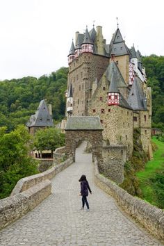 a woman walking across a stone bridge towards a castle