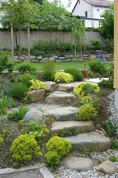 a garden with stone steps leading up to the side of a building and trees in the background