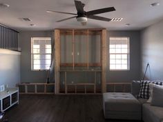 a living room with a ceiling fan and couch in the middle of it, next to a window