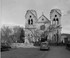 black and white photograph of an old church with cars parked on the street in front