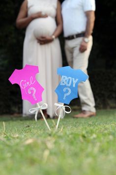 a pregnant couple standing next to each other in the grass with their baby's name on them