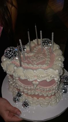 a white cake with pink frosting and disco balls on top is being held by a woman