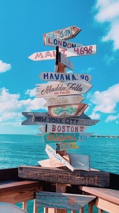 a wooden sign post with many different signs on it's side near the ocean