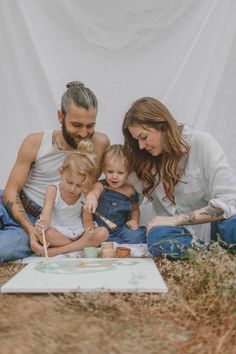 a man, woman and two children sitting on the ground in front of a cake