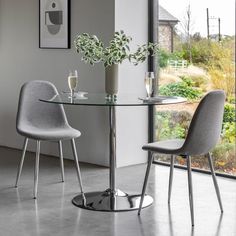 a glass table with two chairs next to it and a vase filled with flowers on top