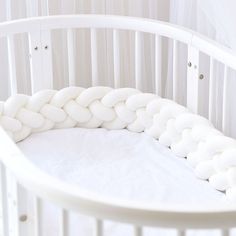 a baby crib with white bedding and pillows on the top of it's sides