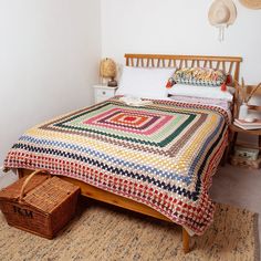 a bed with a colorful quilt on top of it next to a basket and lamp