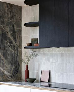 a kitchen with black cabinets and marble counter tops, including a vase on the shelf