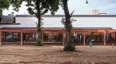 an empty building with trees in the foreground and people walking on the other side