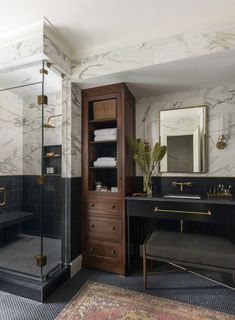 a bathroom with marble walls and flooring has a black vanity, gold accents, and a walk - in shower