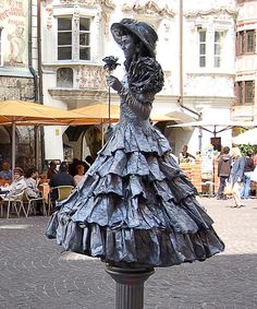 a statue of a woman in a dress on a street corner with people sitting at tables