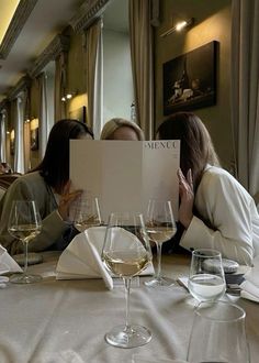 two women sitting at a table with wine glasses in front of them and one woman covering her face