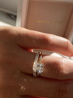 a woman's hand holding a ring with two diamonds on it and a box in the background