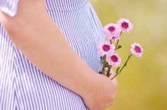 a pregnant woman holding a bouquet of pink flowers in her belly and wearing a blue striped shirt