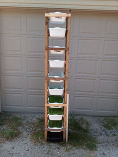 a tall wooden shelf filled with plastic containers and grass in front of a garage door