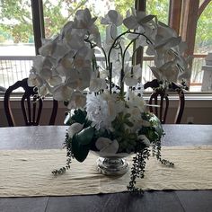 a vase filled with white flowers sitting on top of a table next to a window