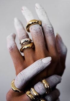 a woman's hand with five gold rings on her fingers and two white nails