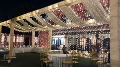 an outdoor wedding venue with white and red lights on the ceiling, tables set up for dinner