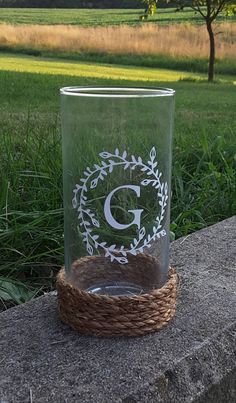 a glass with the letter g on it sitting on a rock in front of some grass